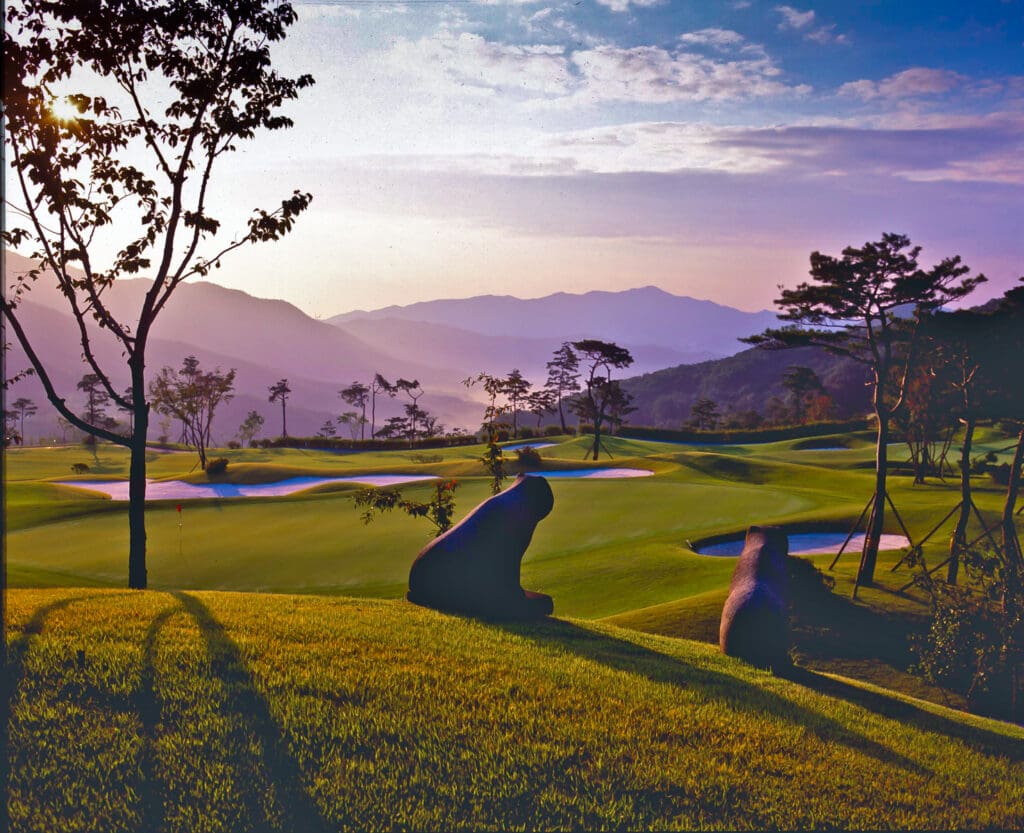 Golf course photograph of East Valley Golf Club near Seoul, South Korea, showing rolling greens, hillside terrain, and stone guardian statues.