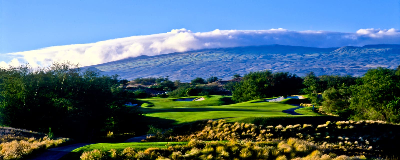 Golf course photograph of Hapuna Golf Club on the Big Island of Hawaii, showing green fairways framed by lava rock and volcanic mountains.