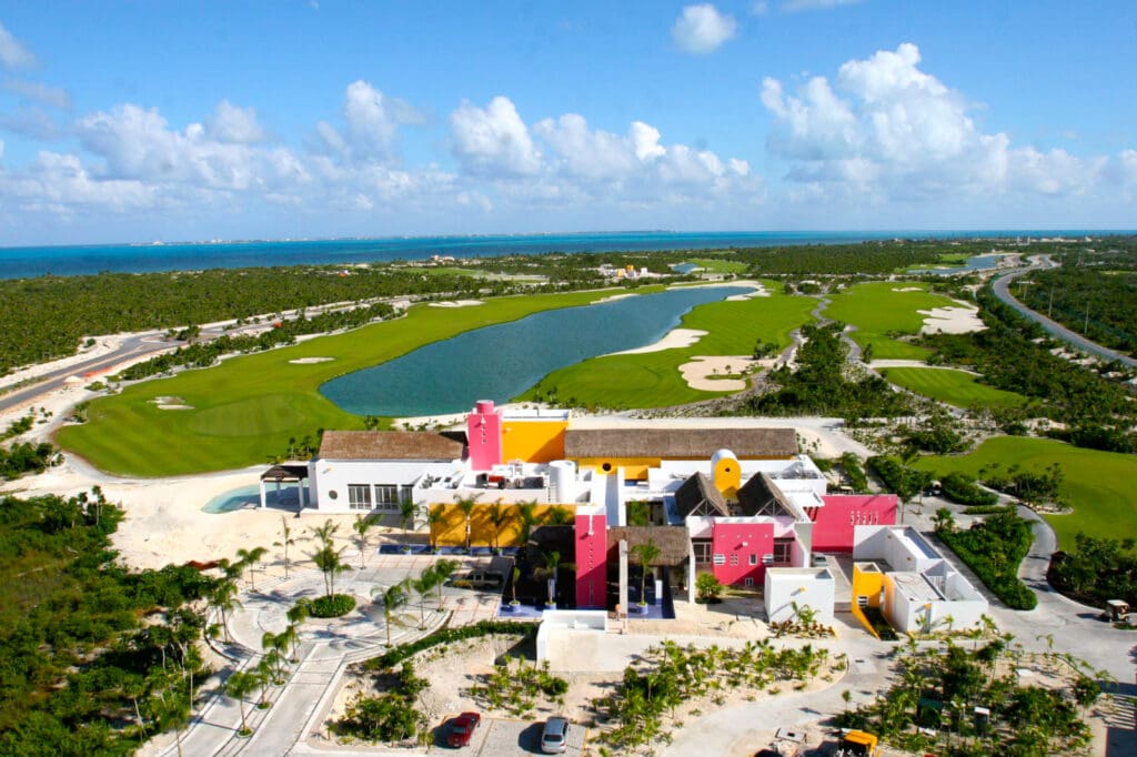 Aerial golf course photograph of Playa Mujeres Golf Club in Quintana Roo, Mexico, showing clubhouse, fairways, water features, and the Caribbean coast.