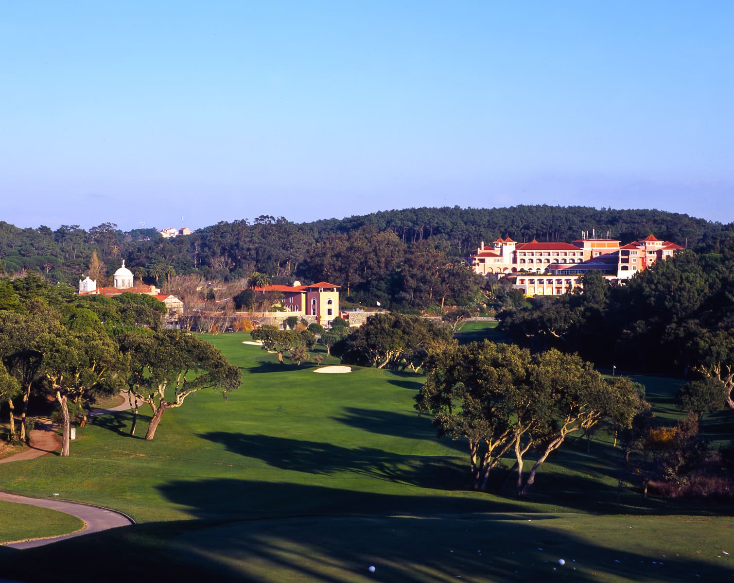 Golf course photograph of Penha Longa Resort in Sintra, Portugal, showing fairways framed by historic buildings and wooded hills.